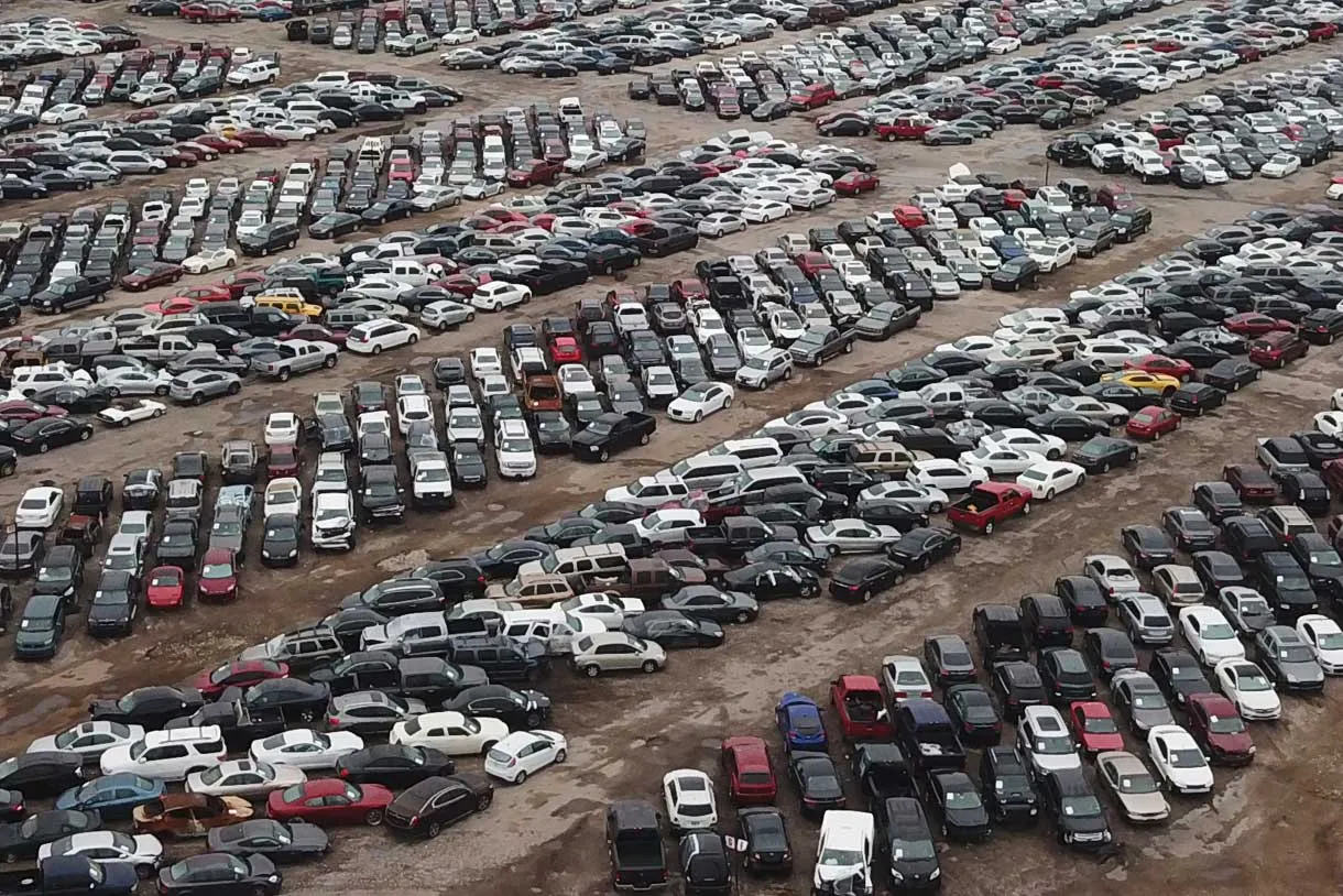 Aerial view of a large auto auction lot filled with rows of parked vehicles arranged across an open dirt yard