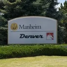 Manheim Denver auto auction entrance sign displayed outdoors with trees and landscaping in the background