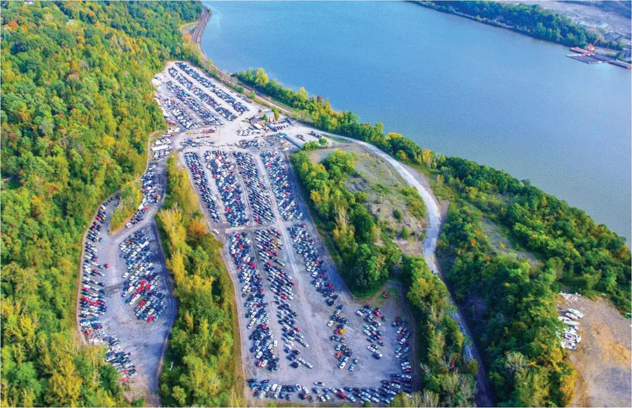 aerial-view-of-a-large-auto-auction-yard-surrounded-by-trees-and-water-with-hundreds-of-vehicles-parked-for-sale