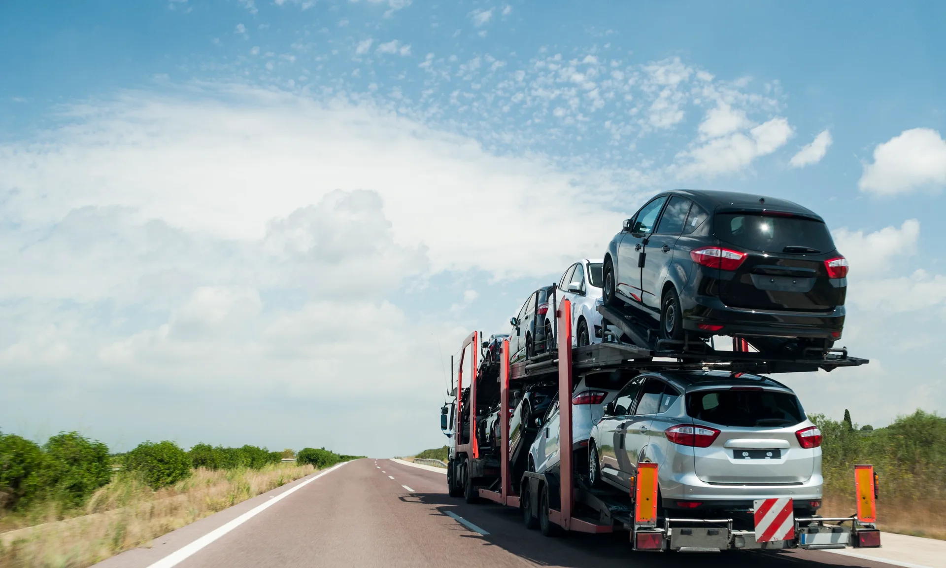 Multi-car auto transport trailer carrying several vehicles on a highway under a clear sky during long-distance vehicle shipping