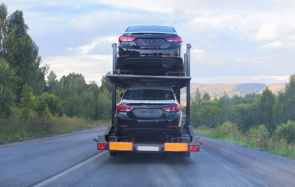 two-cars-loaded-on-an-auto-transport-trailer-seen-from-the-rear-driving-on-a-rural-road-during-long-distance-shipping