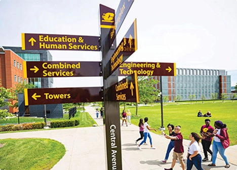 students walking past directional sign on university campus grounds