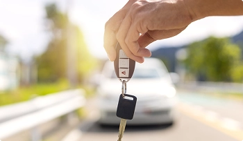 hand holding car keys with blurred car in background for safe delivery