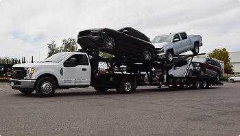 White truck hauling multiple cars on an open carrier in a parking lot