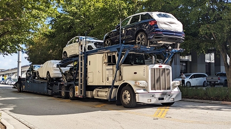 white semi car hauler transporting wrapped suvs on a city street for dealership delivery